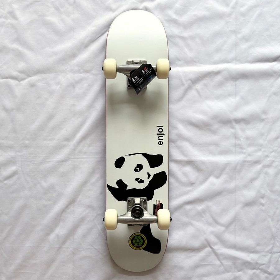 Compact skateboard with a panda graphic, silver trucks, and cream wheels viewed from above on white fabric.