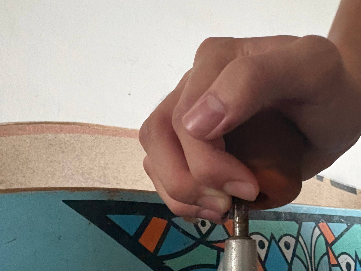 A close-up of a hand using the axle of a skateboard truck to pry a bearing out of a wheel.